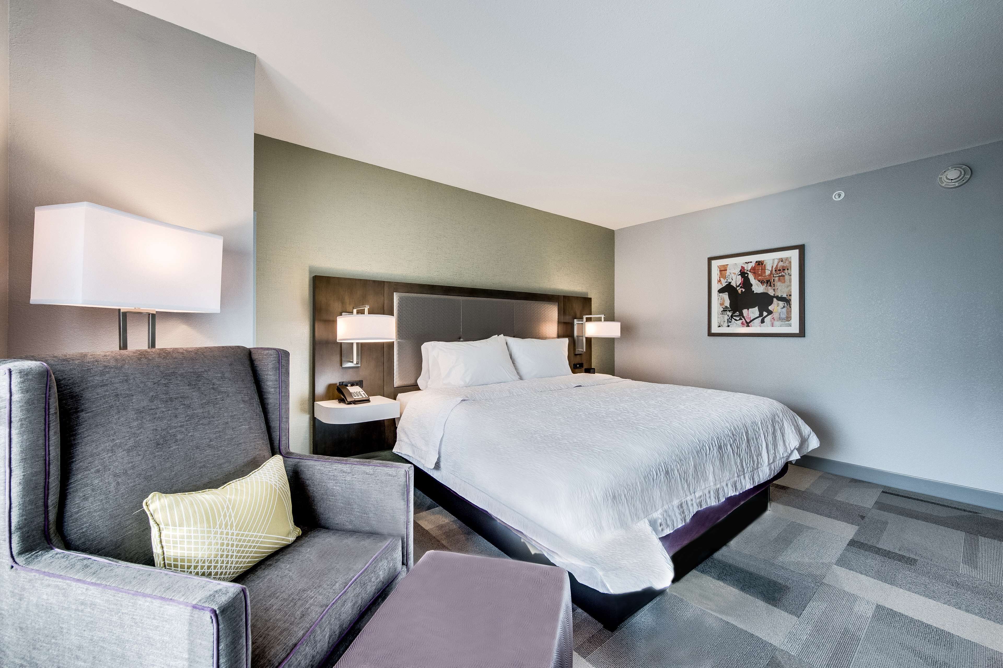 A modern hotel room with a large bed, a sofa, and a nightstand with a lamp.