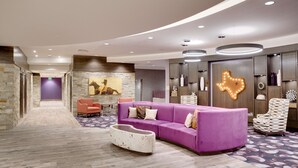 A modern lobby with a purple sofa, a patterned rug, and a stone wall. - Hampton Inn & Suites Fort Worth Downtown (Fort Worth)