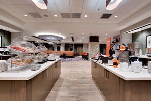 Zona de desayuno en el hotel, con estaciones de autoservicio, asientos y vista al vestíbulo.