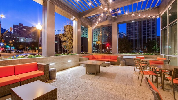 An outdoor patio area with seating and tables, large windows, and string lights. - Hampton Inn & Suites Fort Worth Downtown (Fort Worth)