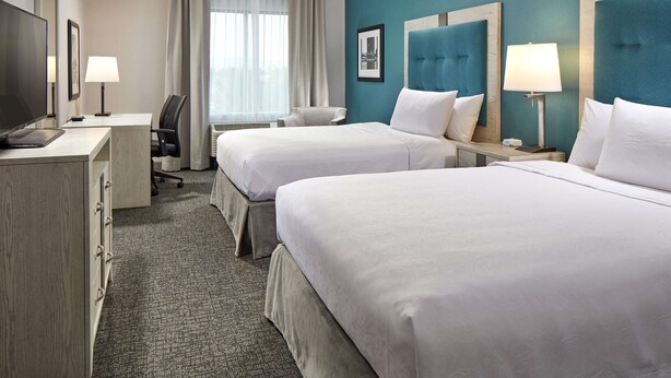 Une chambre d’hôtel avec deux lits, un bureau, une chaise, une télévision et une fenêtre avec des rideaux.