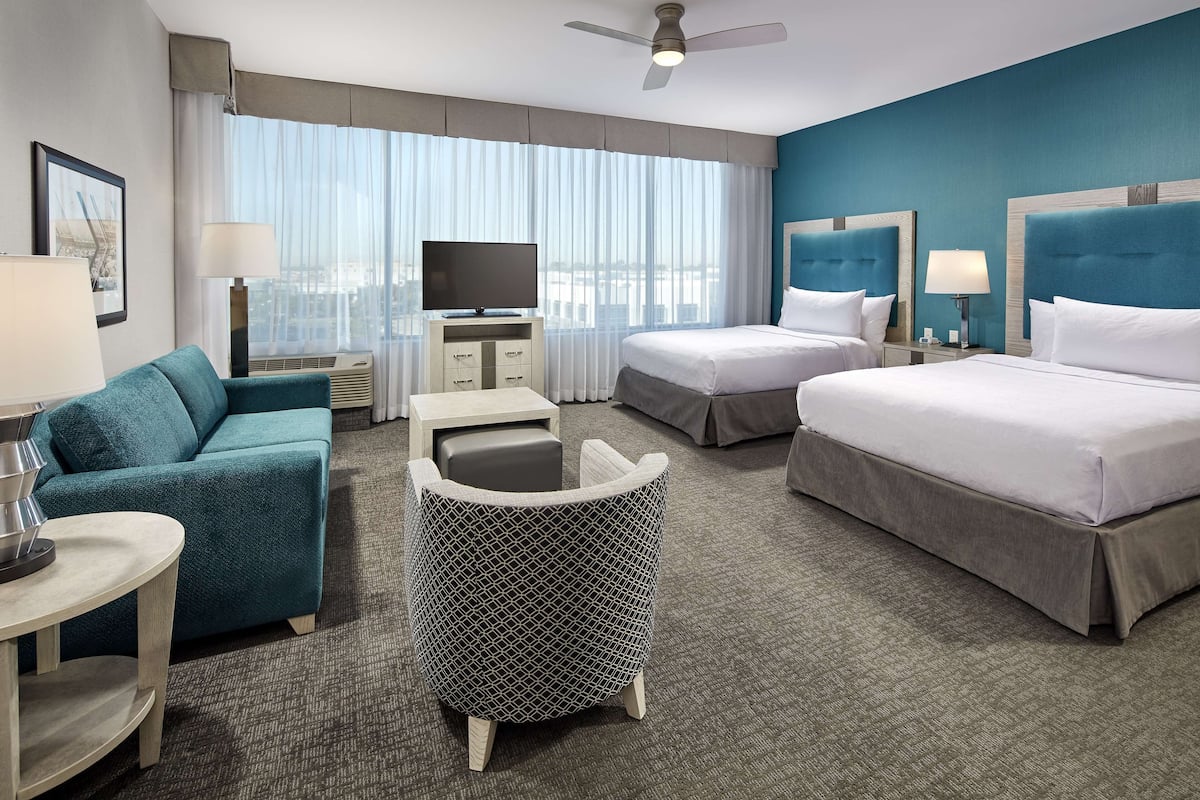 A hotel room with two beds, a sofa, a small table, a TV, and a window with curtains.