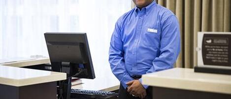 A hotel reception desk with a computer, a name tag, and a sign with text.