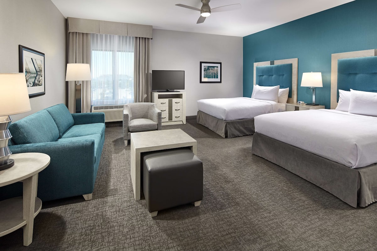 A hotel room with two beds, a sofa, a desk, a chair, a TV, and a window with curtains.