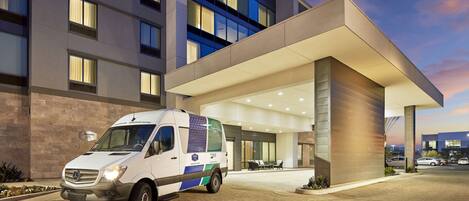 A modern hotel entrance with a white van parked in front.