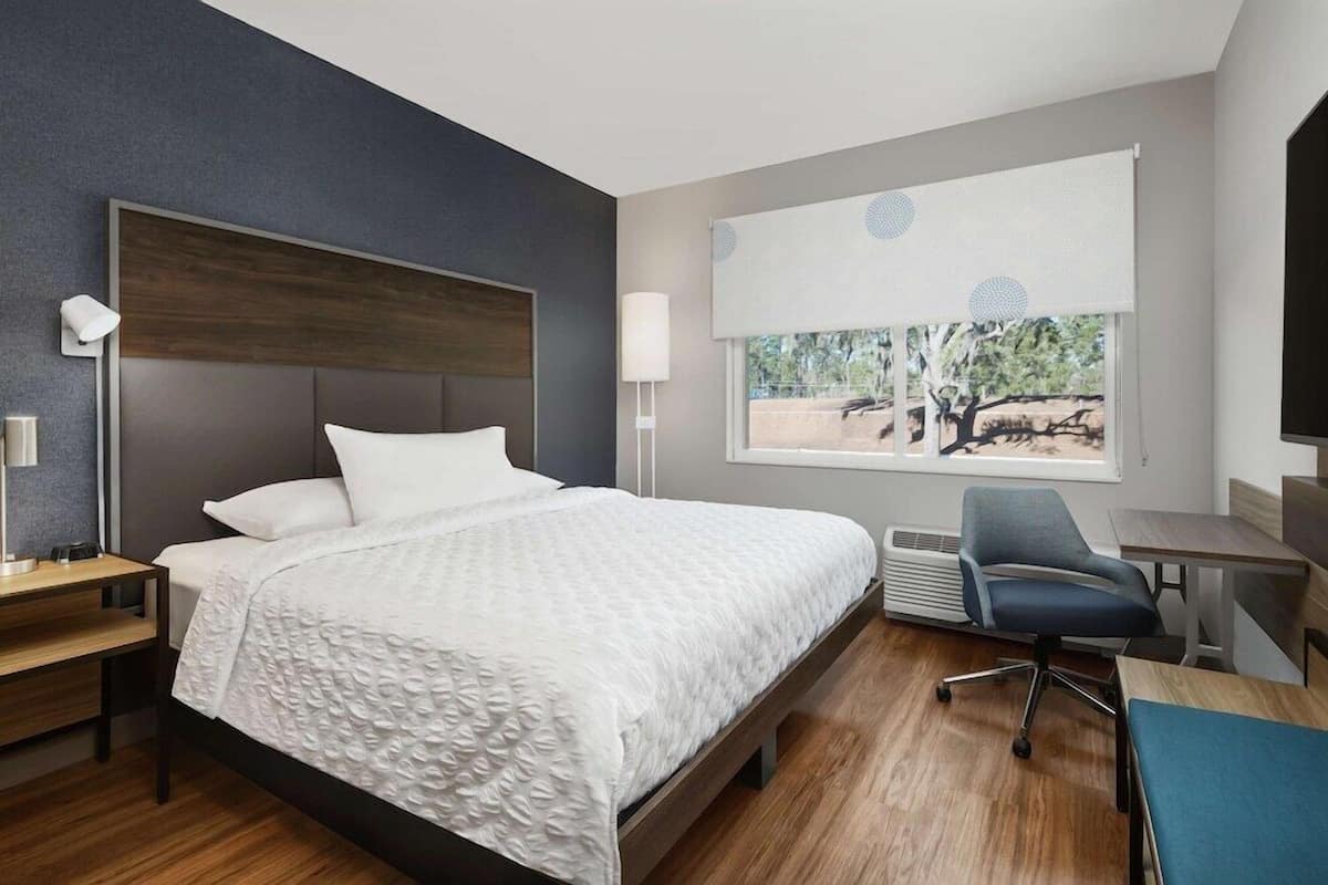 Une chambre d’hôtel moderne, dotée d’un grand lit, d’un bureau, d’une chaise et d’une fenêtre donnant sur la verdure.