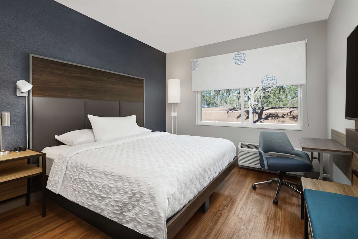Une chambre d’hôtel moderne dotée d’un grand lit, de tables de chevet, d’un bureau, d’une chaise et d’une fenêtre donnant sur des arbres.