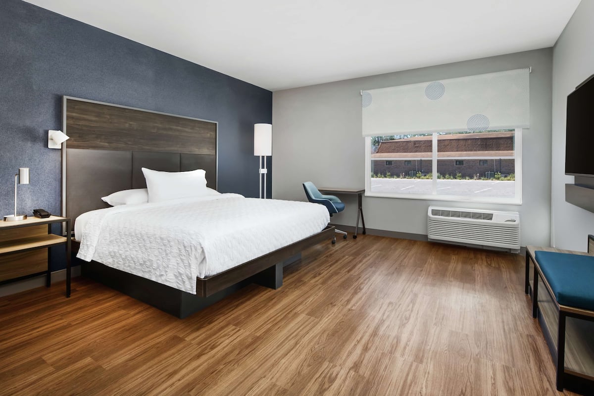 Une chambre d’hôtel moderne, dotée d’un grand lit, de tables de chevet, d’un bureau, d’une chaise, d’une télévision et d’une fenêtre donnant sur un parking.