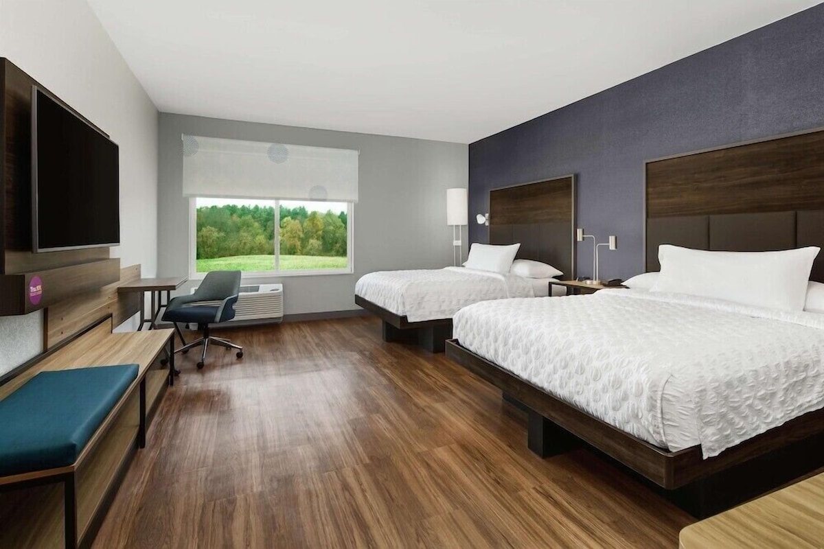 A hotel room with two beds, a TV, a desk, and a chair.