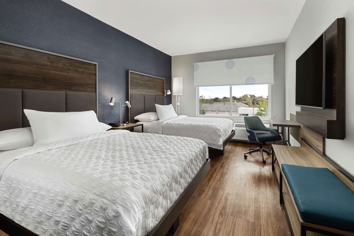 Une chambre d’hôtel avec deux lits, un bureau, une chaise, une télévision et une grande fenêtre.