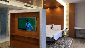 Une chambre d’hôtel moderne avec un plafond en bois, un grand téléviseur à écran plat fixé sur un panneau en bois, un lit avec du linge de maison blanc et une petite table de chevet.