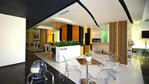 Un hall d'entrée moderne avec un espace lounge-café, des chaises en verre transparent et un comptoir d'accueil.