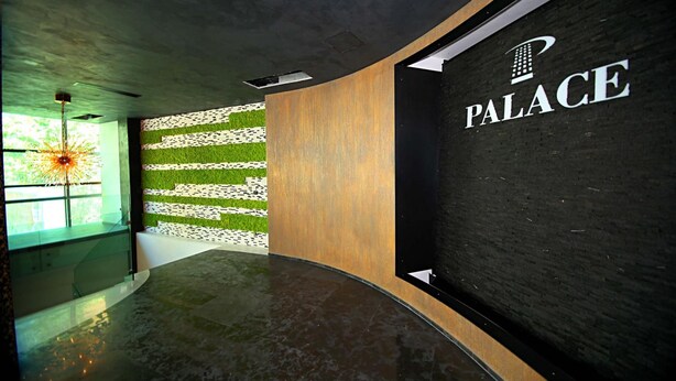 Un espace d’accueil moderne avec un comptoir d’accueil incurvé, une enseigne murale indiquant « PALACE » et un mur recouvert de gazon artificiel vert.