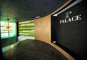 A modern reception area with a curved reception desk, a wall-mounted sign reading "PALACE," and a green artificial grass wall. - Hotel Palace Vlore (Vlorë)