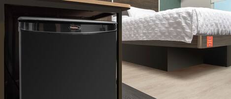 Un refrigerador compacto negro en una habitación de hotel, con cama y cabecera de madera.