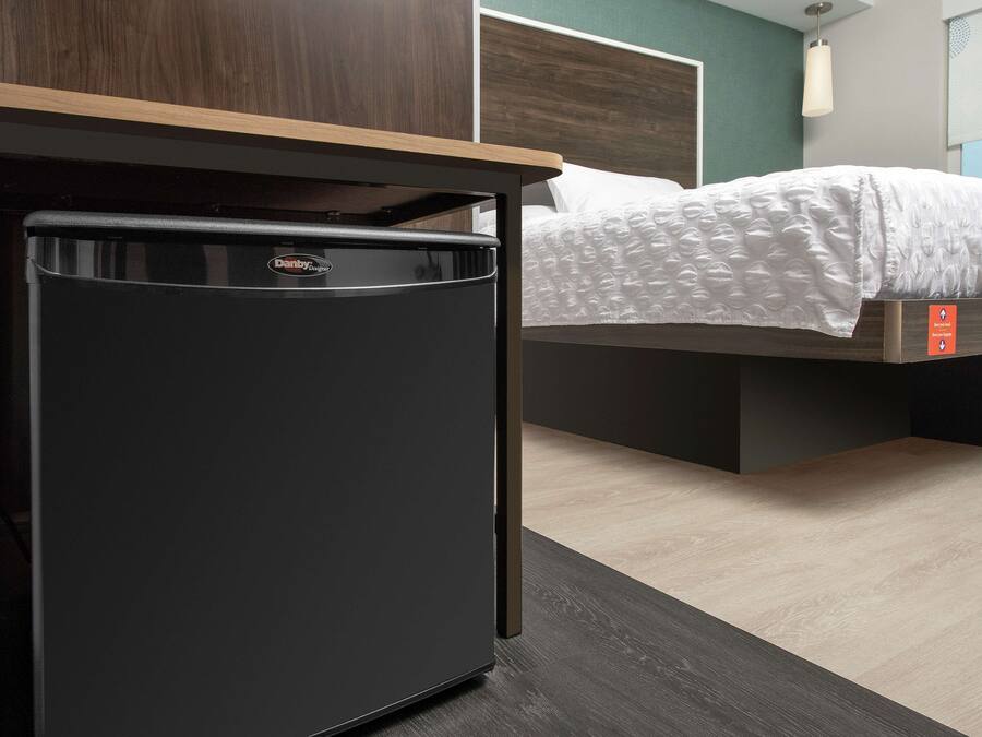 A compact black refrigerator in a hotel room with a bed and a wooden headboard.
