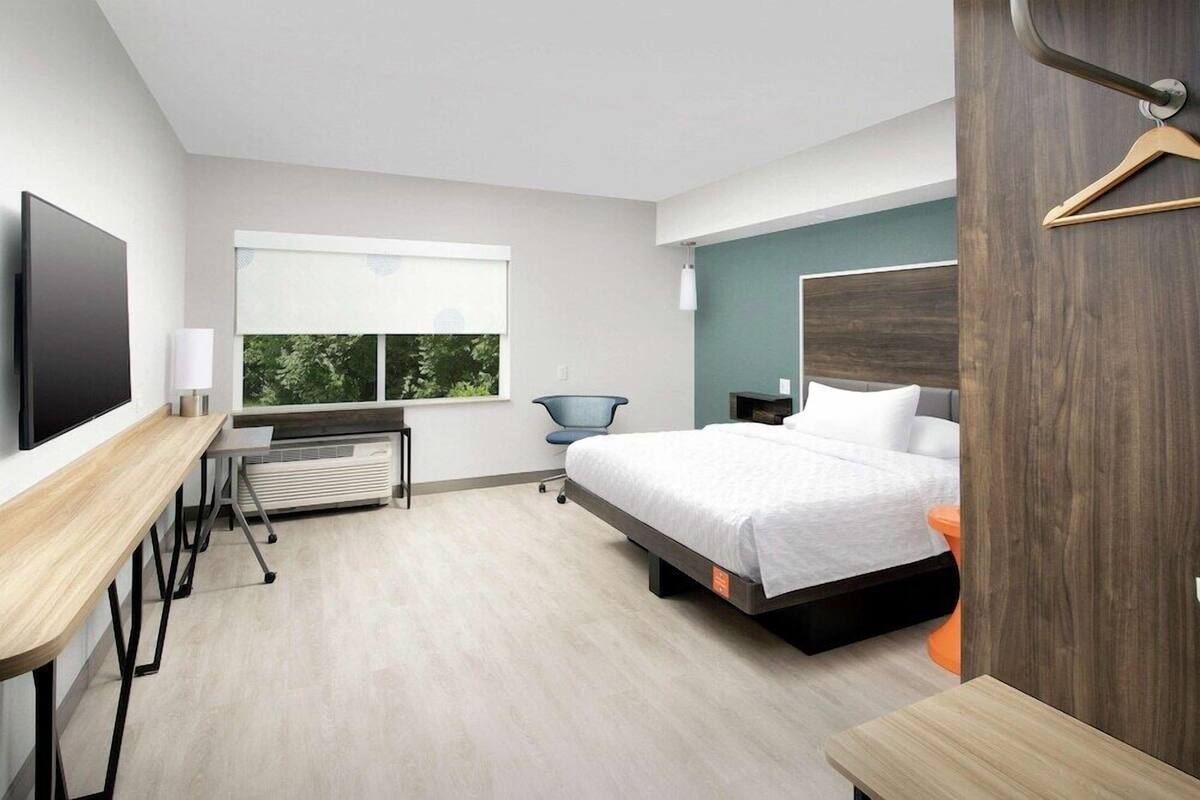 Ein modernes Hotelzimmer mit Bett, Schreibtisch, Stuhl und Fernseher.