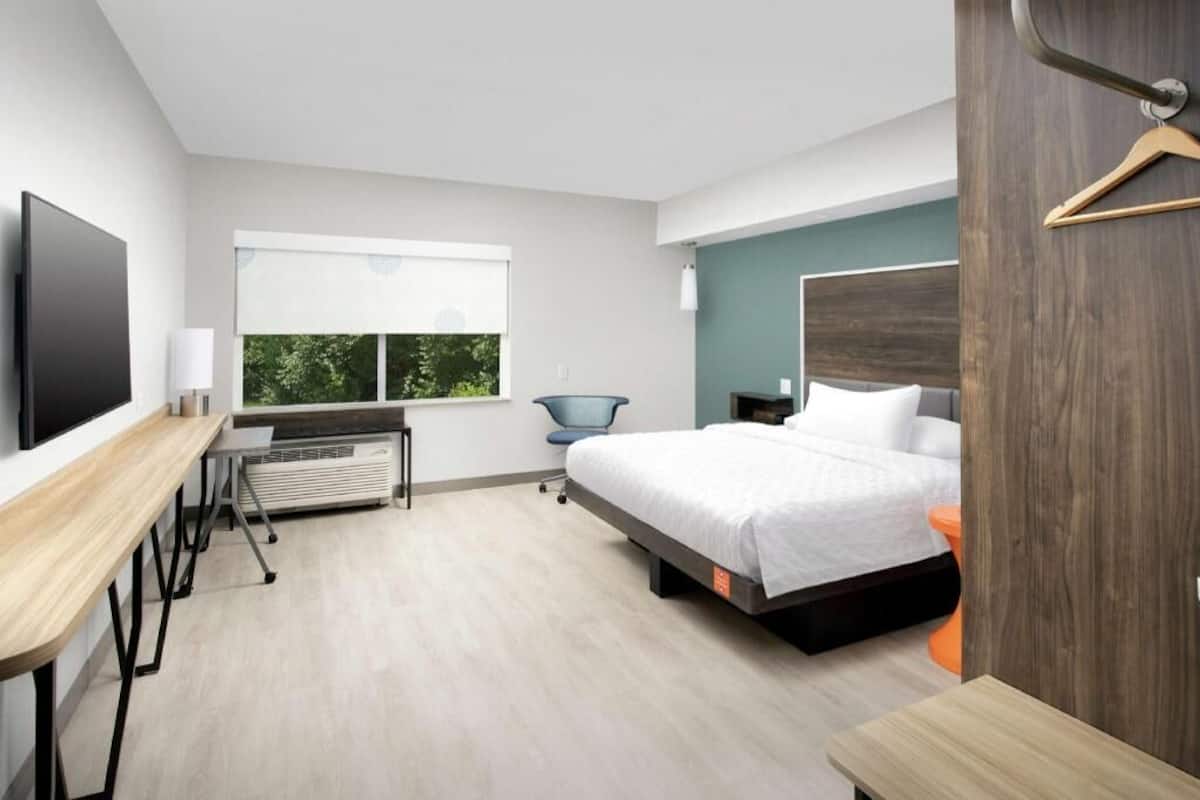 Ein modernes Hotelzimmer mit Bett, Schreibtisch, Stuhl und Fernseher.