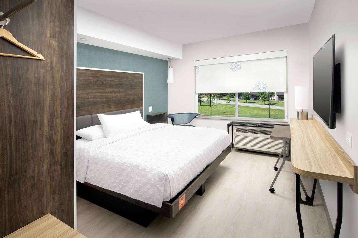 Ein modernes Hotelzimmer mit einem großen Bett, einem Schreibtisch und Blick auf einen grünen Park durch das Fenster.
