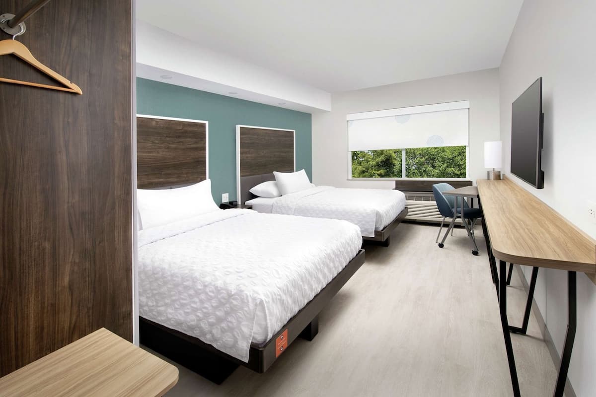 Ein modernes Hotelzimmer mit zwei Betten, einem Schreibtisch und einem großen Fenster mit Blick auf Grünflächen.