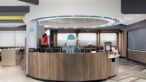 A modern hotel reception area with a wooden reception desk, a digital screen, and a view of the outdoors. - Tru by Hilton Louisville East (Louisville)