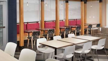 A modern dining area with wooden tables and white chairs, red cushioned seating, and pendant lighting.