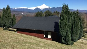 A cabin with a metal roof, surrounded by tall trees and a mountain in the background. - Cabañas en Pucon con vista cordillera (Pucón)