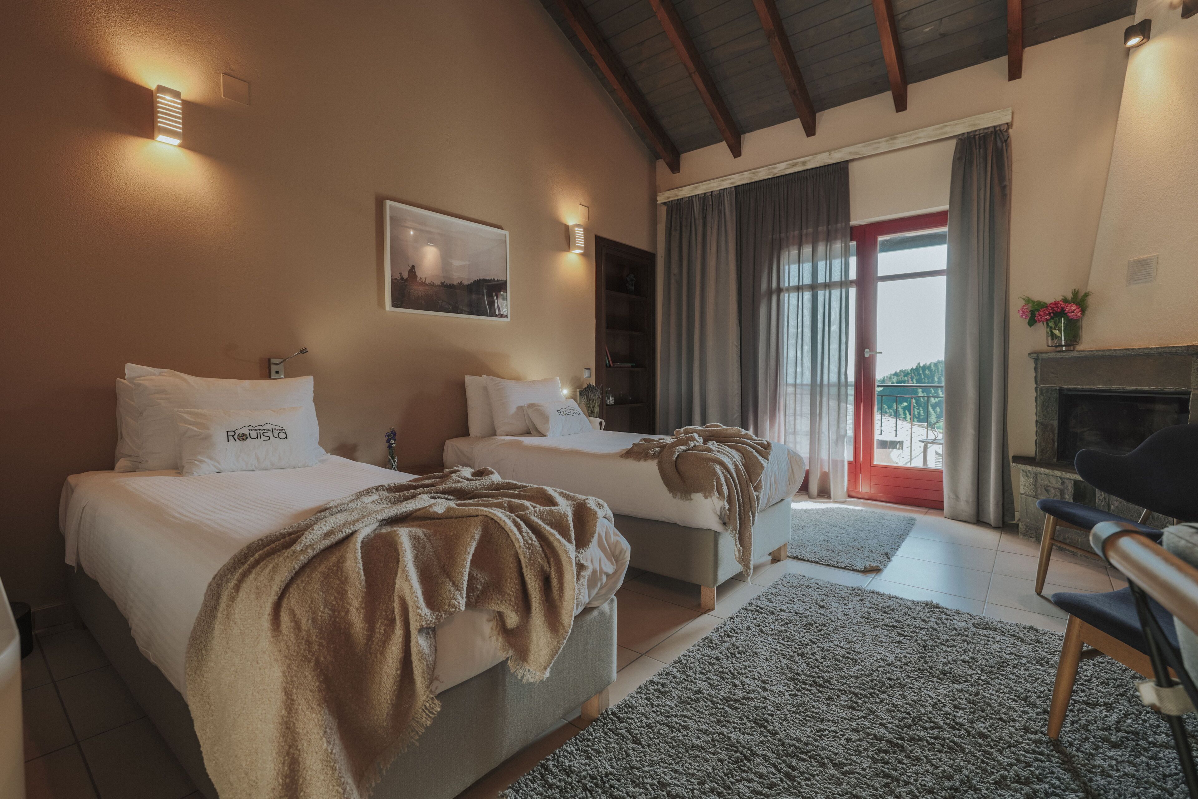 A hotel room with two beds, a fireplace, a large window with curtains, and a view of the outdoors.