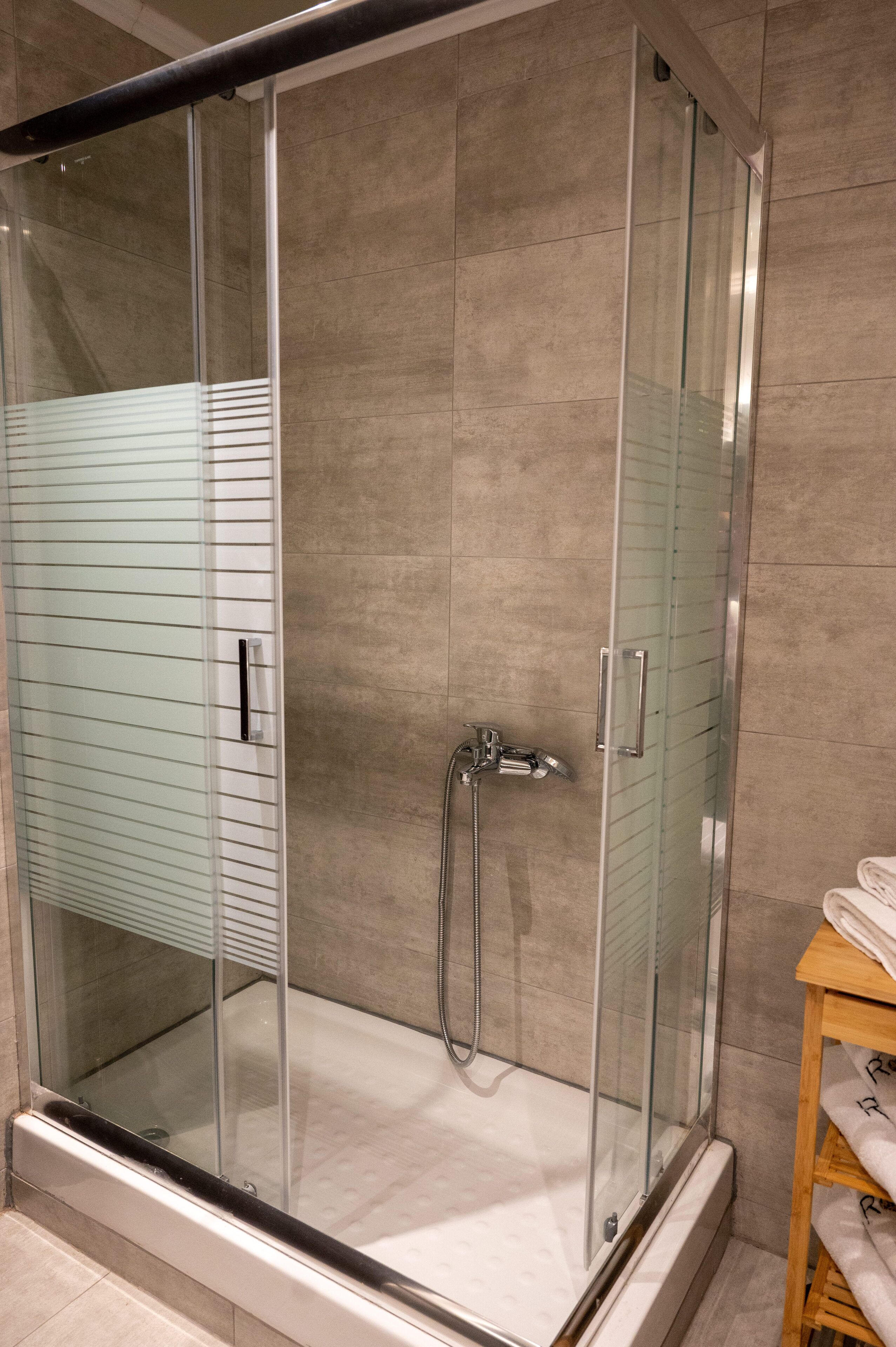 A glass-enclosed shower stall with a handheld showerhead and a wall-mounted faucet.