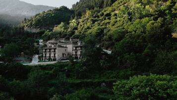 A traditional stone building with multiple balconies, surrounded by dense forest and a mountain in the background.