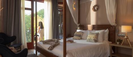 Een slaapkamer met een hemelbed, nachtkastje met een lamp en uitzicht op het omliggende landschap.