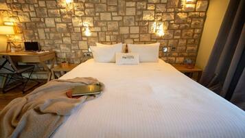 Habitación de hotel con pared de piedra, cama con ropa de cama blanca, escritorio con una computadora portátil y una manta en el suelo.