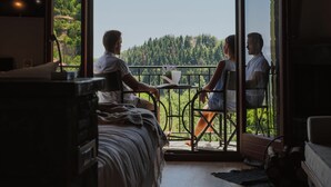 A room with a bed, a table, and a view of a forest through a glass door. - Rouista Tzoumerka Resort (Central Tzoumerka)