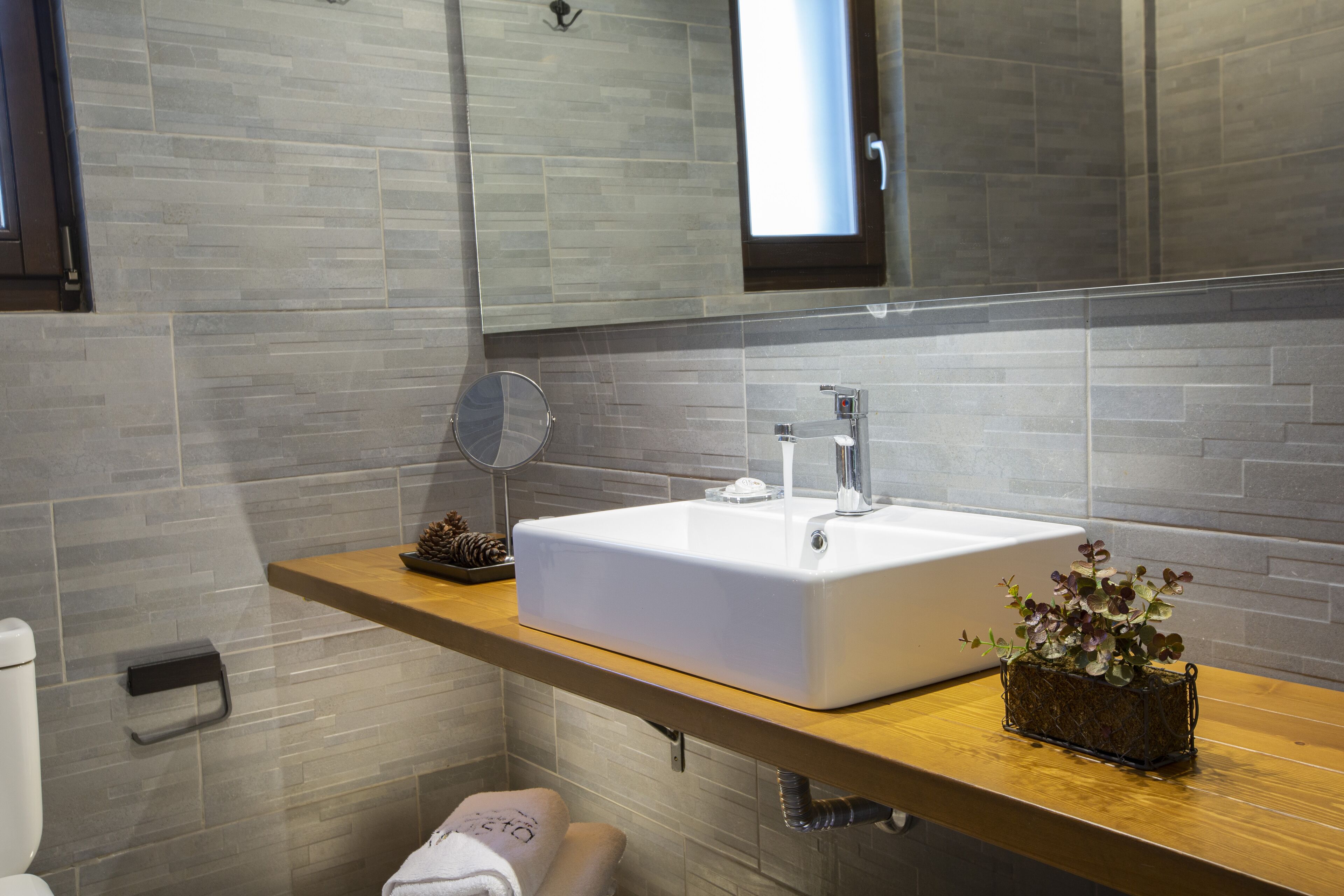 Ein modernes Badezimmer mit einem großen weißen Waschbecken, einer Holz-Arbeitsplatte, einem Spiegel und einem Blumentopf.