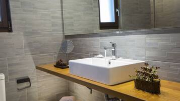 Ein modernes Badezimmer mit einem großen weißen Waschbecken, einer Holz-Arbeitsplatte, einem Spiegel und einem Blumentopf.