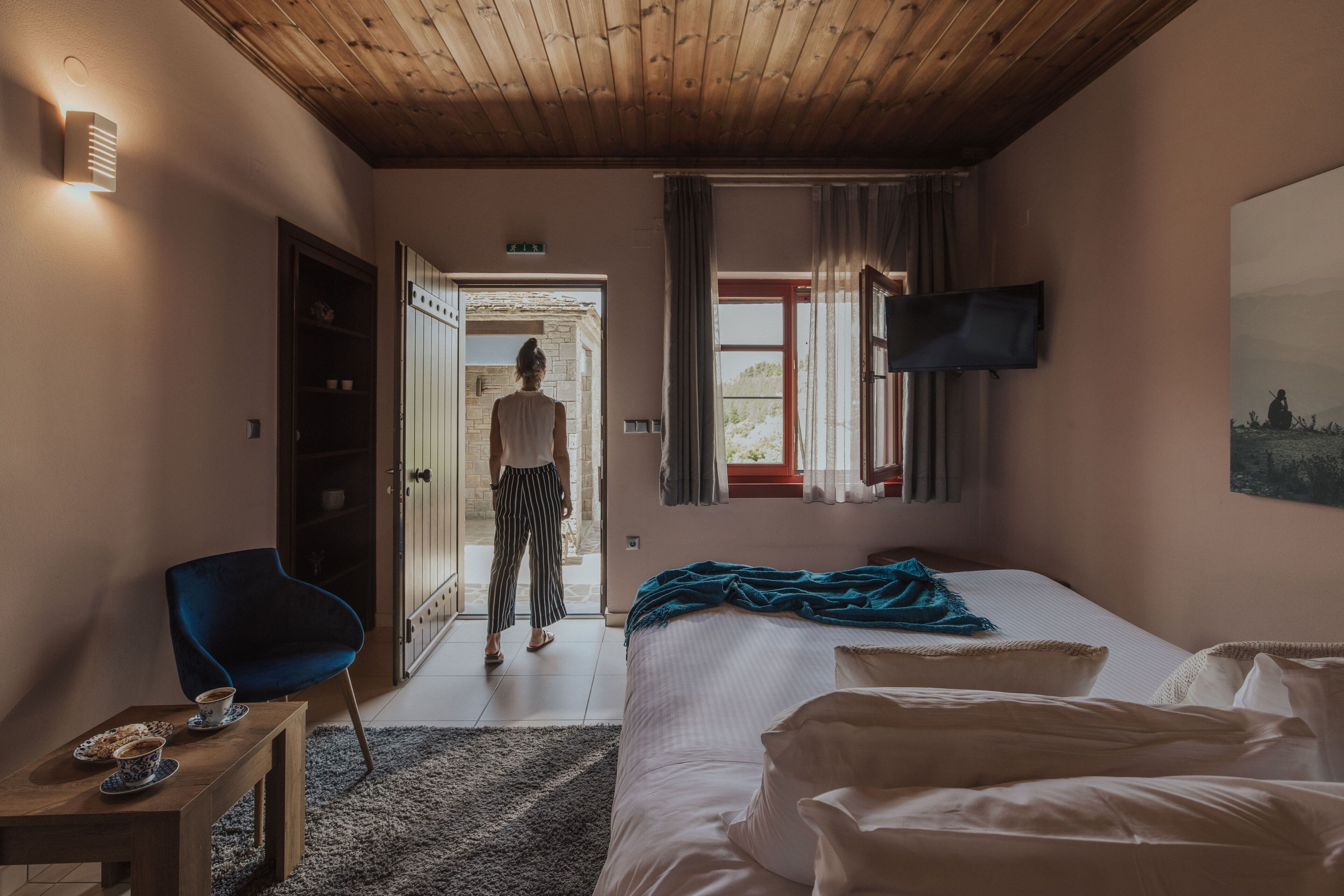 A hotel room with a bed, a TV, a wooden ceiling, and a view of the outdoors.