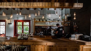 A bar area with wooden furniture, hanging light bulbs, and shelves with bottles and glasses. - Rouista Tzoumerka Resort (Central Tzoumerka)