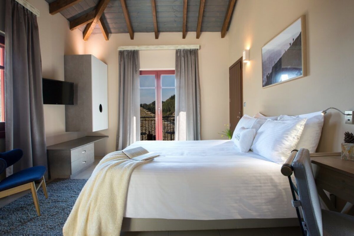 A bedroom with a bed, a desk, a chair, a TV, and a window with curtains.
