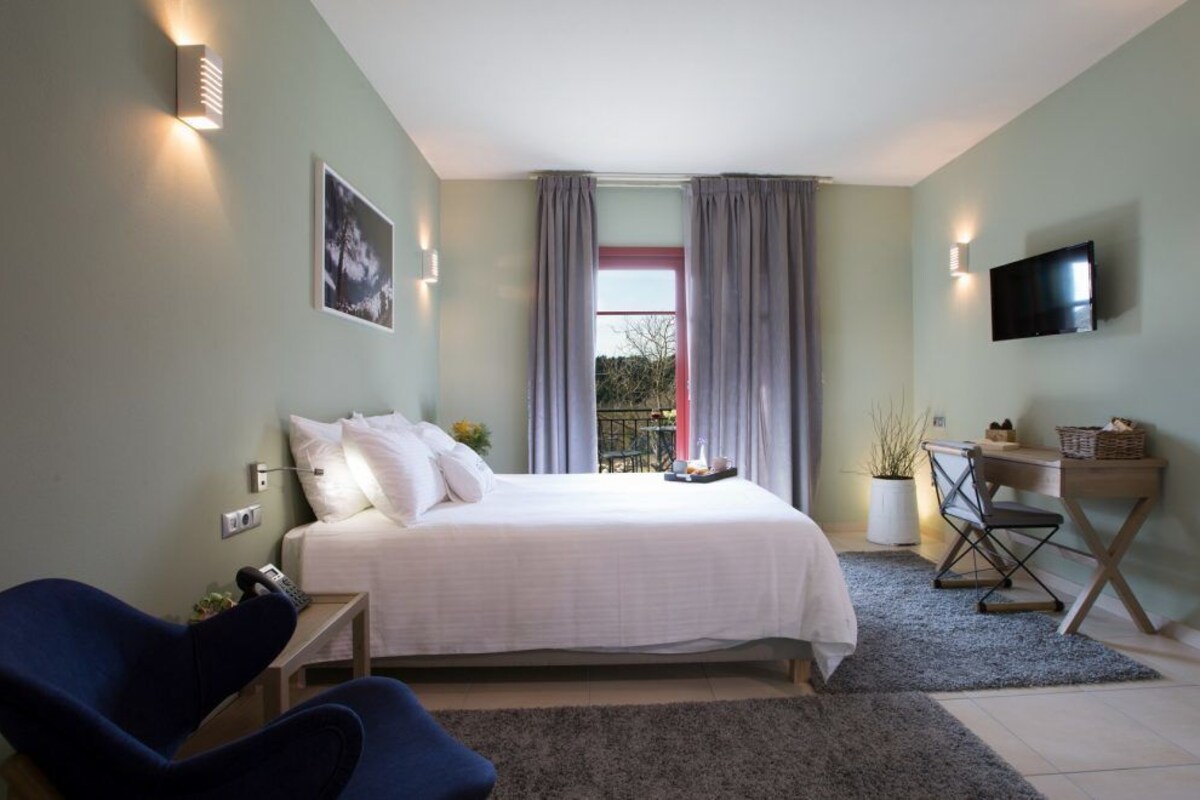 A bedroom with a bed, a desk, a chair, a TV, and a window with curtains.