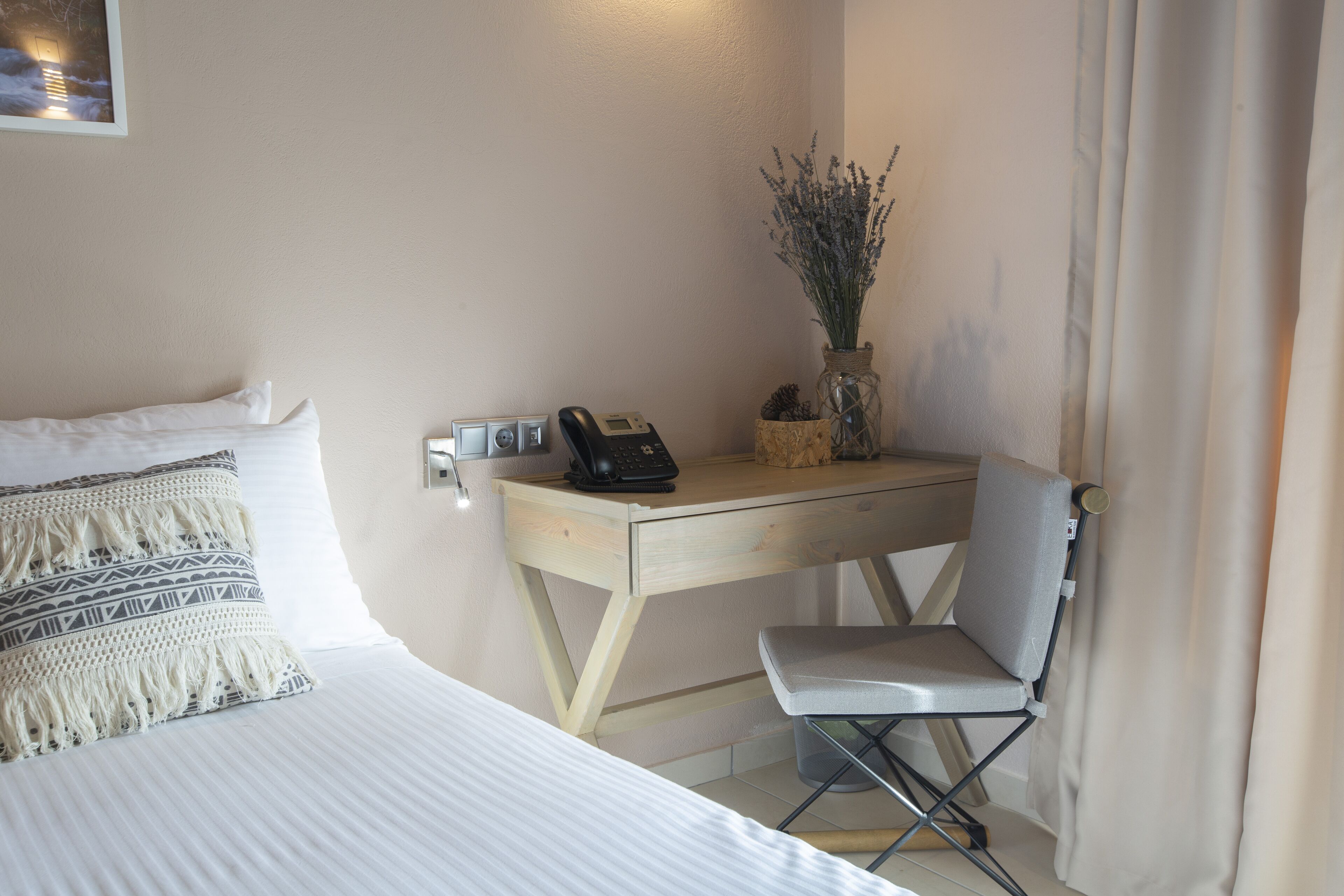 Un dormitorio con una cama, un escritorio, una silla, un teléfono y un florero con plantas.