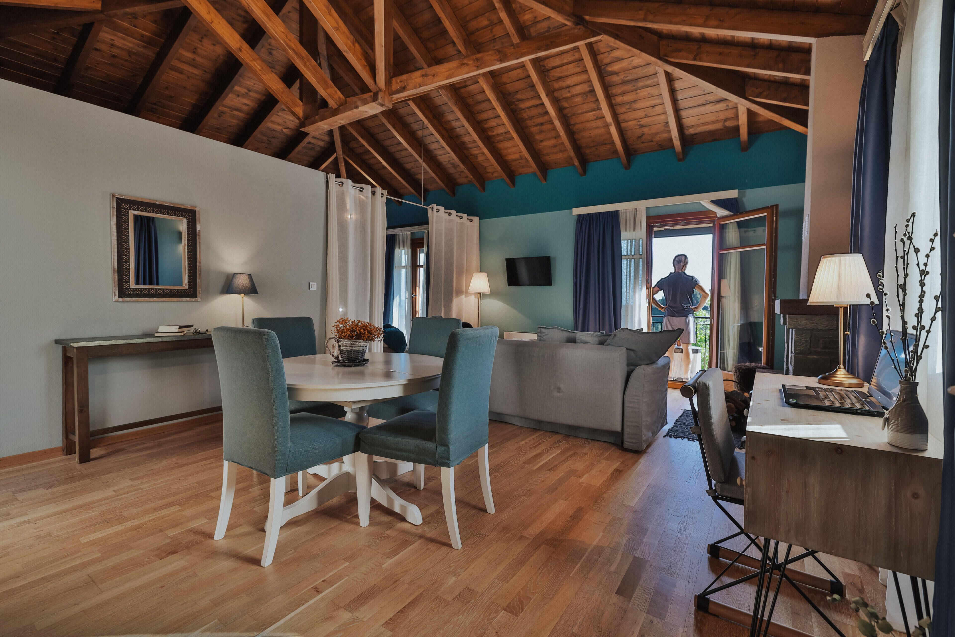 Una habitación amplia con techo de madera, una mesa de comedor con sillas, un sofá y un escritorio con una computadora.