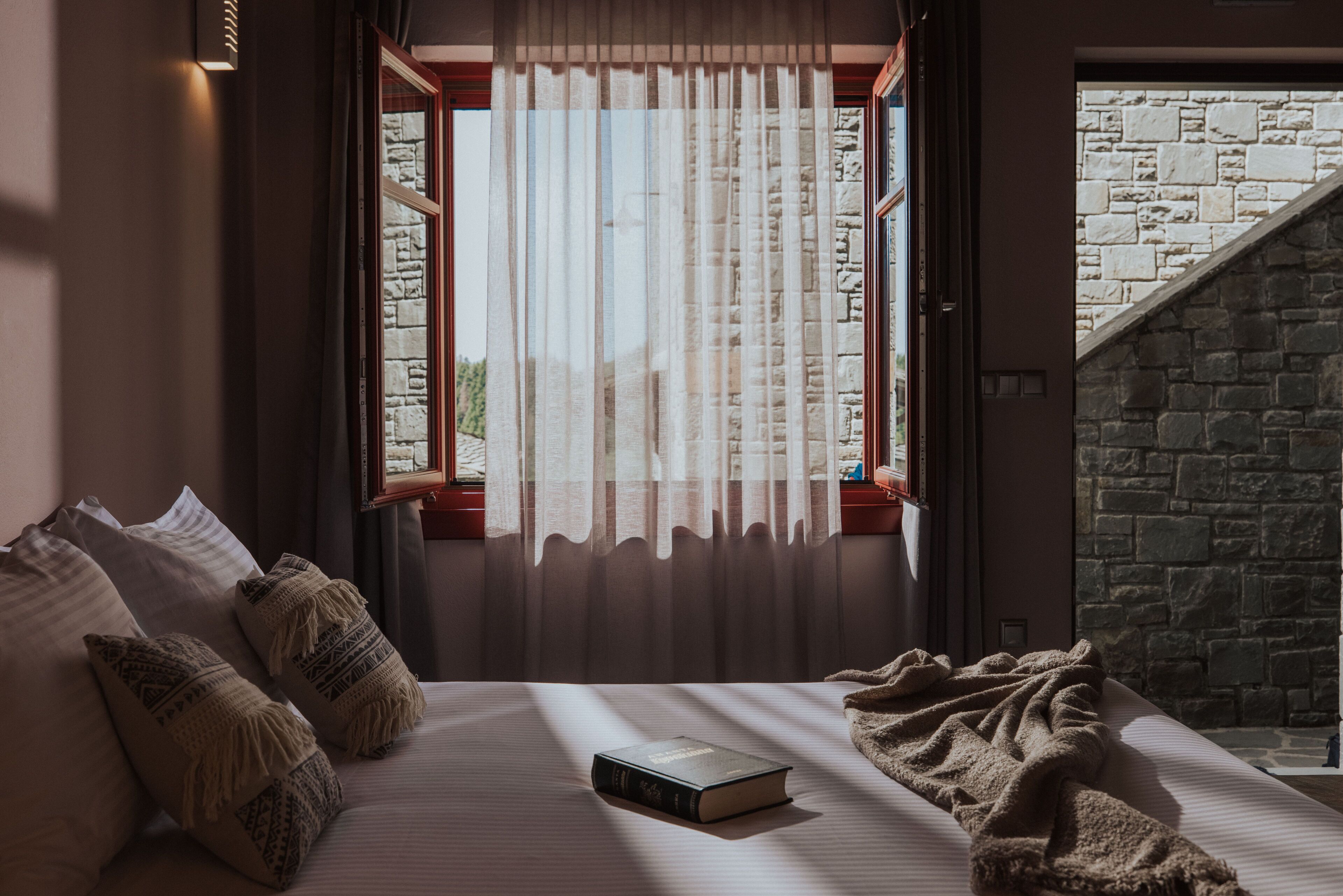 A bedroom with a bed, pillows, a book, and a window with curtains.