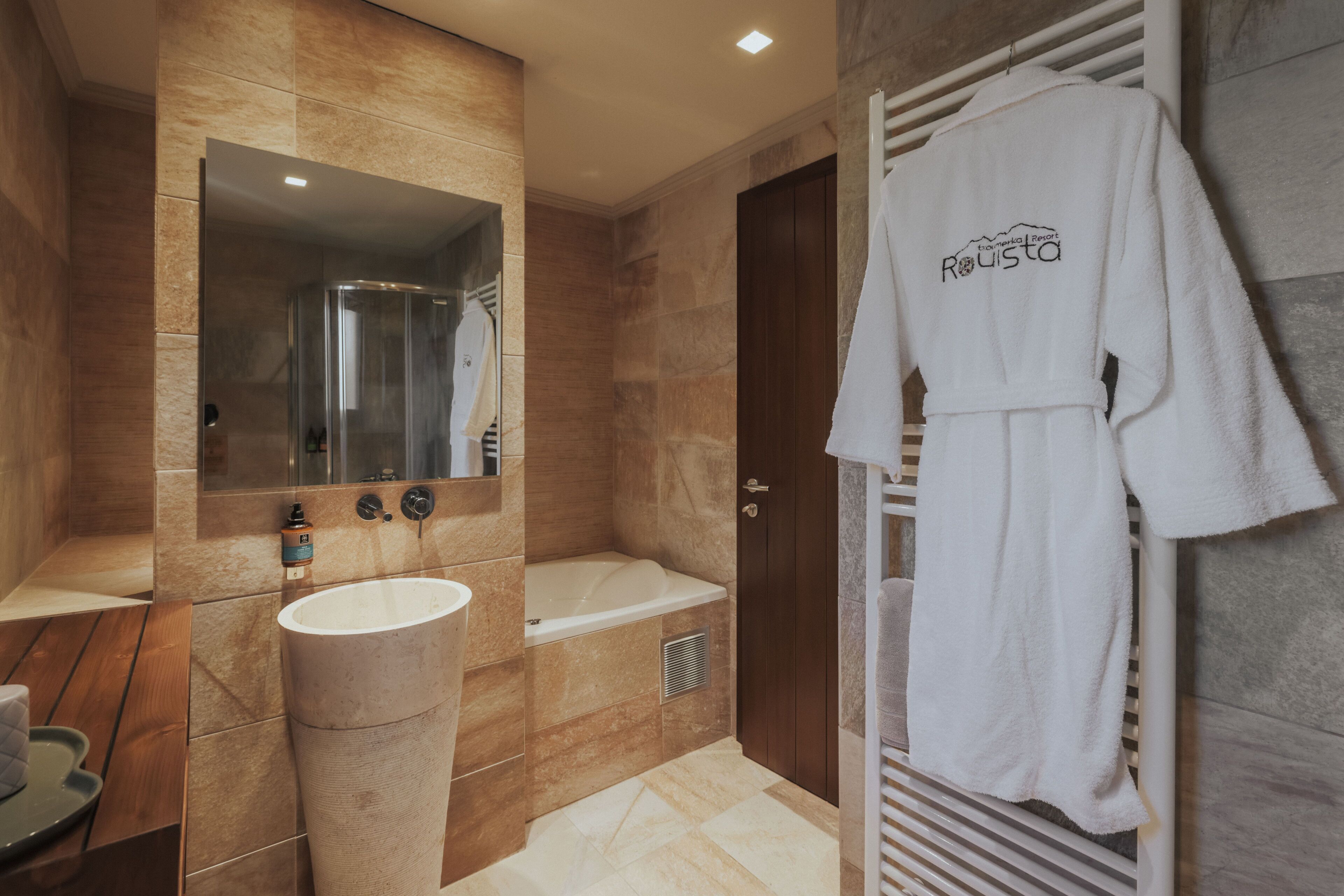 Un baño moderno con bañera, un espejo grande, un lavabo y un perchero con una bata.