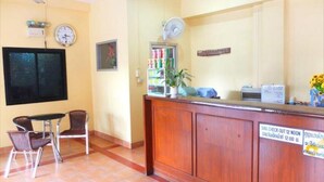A reception area with a wooden desk, two chairs, a clock, a fan, and a sign indicating check-out time. - Utid Court (Pattaya)