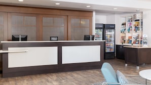 Een hotel receptie met een balie, een minibar, een koelkast en een presentatie van snacks en drankjes.