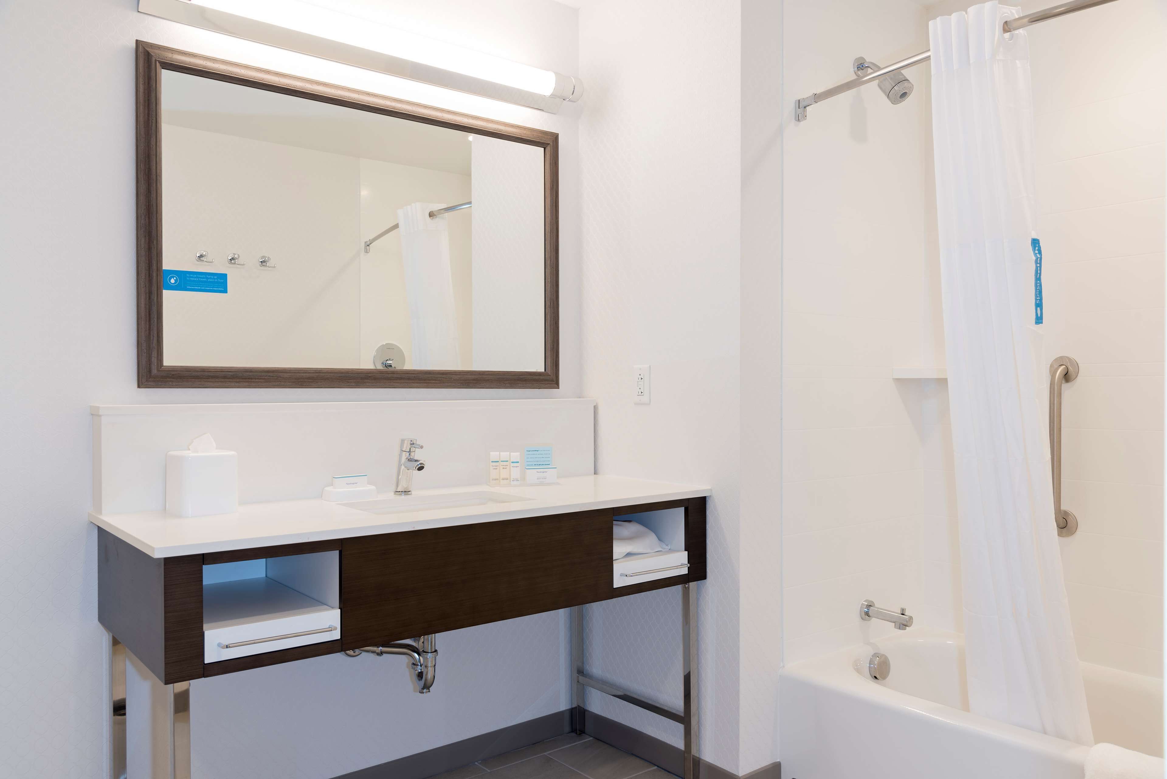 A bathroom with a white sink, dark wooden vanity, a mirror, a shower with a white curtain, and a bathtub.