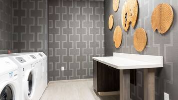 A laundry room with a washing machine, a sink, and decorative woven mats on the wall.