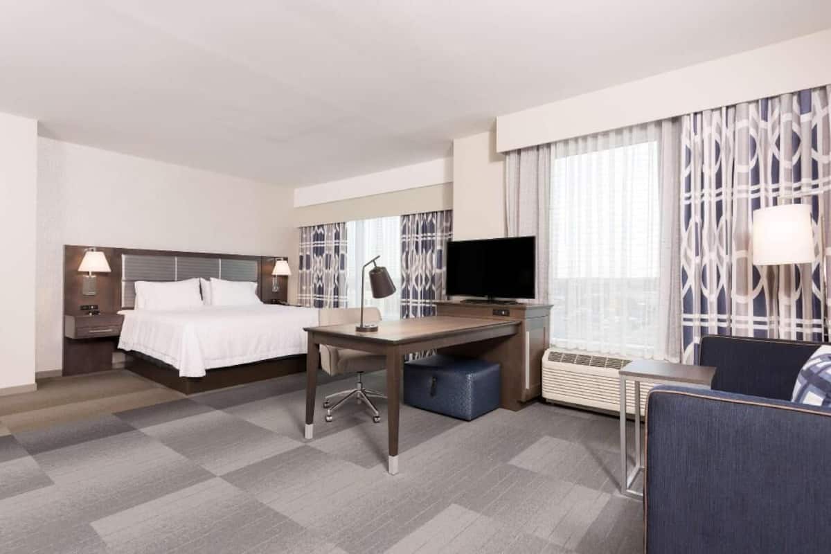 A hotel room with a bed, desk, TV, and a seating area.