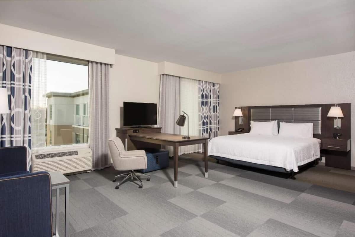 A hotel room with a bed, desk, chair, TV, and a window with curtains.