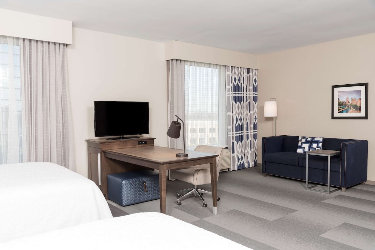 A hotel room with a bed, a desk with a TV, a sofa, and a lamp.